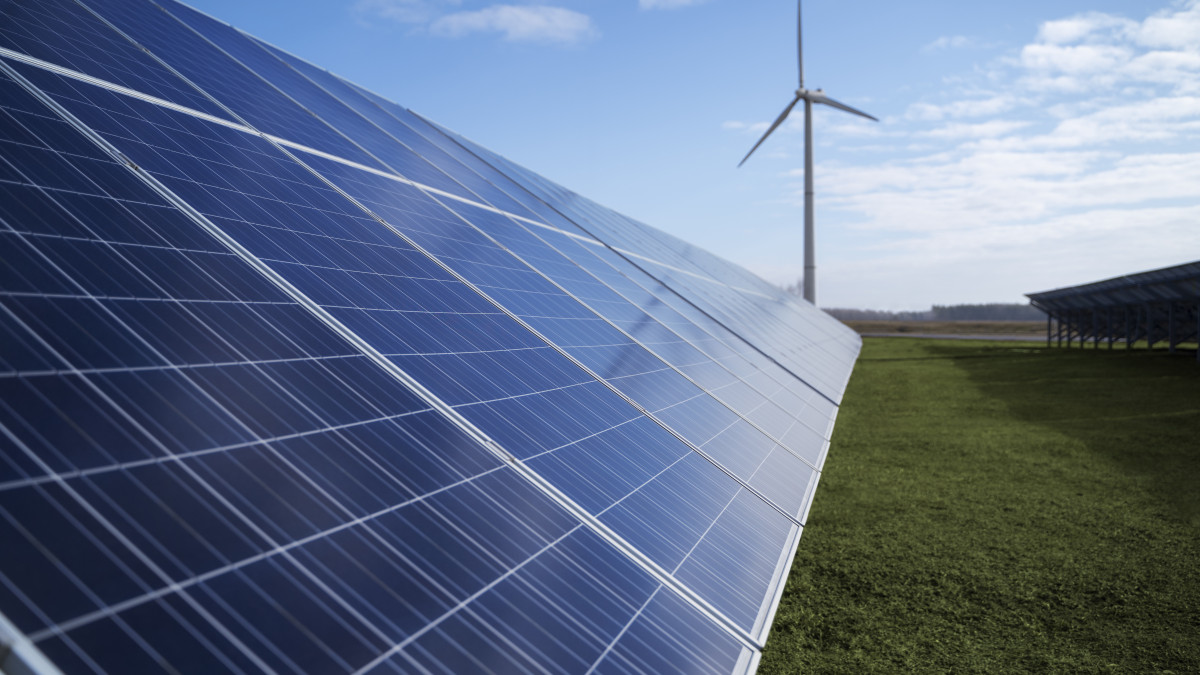 des panneaux photovoltaïque posés sur une pelouse, eolienne en arrière plan dans un ciel bleu.